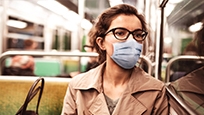 A woman sitting on a bus wearing a blue non medical face mask. 